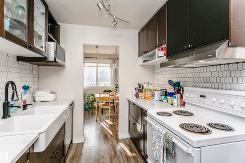 Kitchen with backsplash, stainless steel appliances, dark wood finish cabinetry, glass fronted cabinets, and open shelves - 407 8149 111 St S, Edmonton, AB - Indoor Photo Showing Kitchen With Double Sink