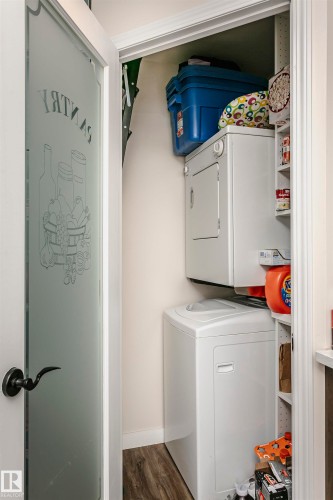 Laundry room featuring stacked washer and clothes dryer and dark wood-style floors - 407 8149 111 St S, Edmonton, AB - Indoor Photo Showing Laundry Room