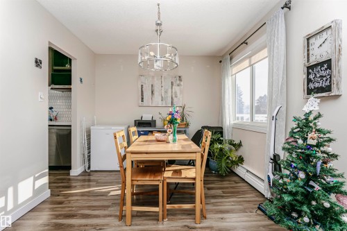 Dining space with wood finished floors, a chandelier, a baseboard radiator, and wine cooler - 407 8149 111 St S, Edmonton, AB - Indoor Photo Showing Dining Room