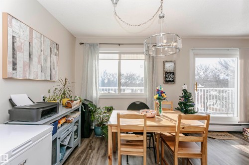 Dining space with dark wood-style flooring, healthy amount of natural light, suspended lighting, and a baseboard heating unit - 407 8149 111 St S, Edmonton, AB - Indoor Photo Showing Dining Room