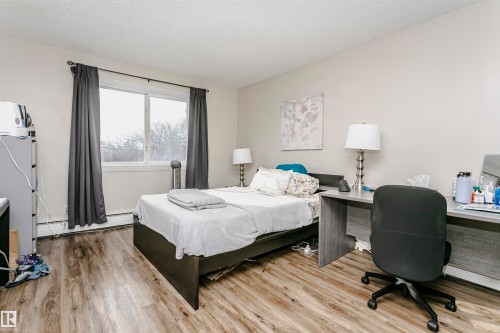Bedroom featuring light wood-style flooring, baseboard heating, a textured ceiling, and an office area - 407 8149 111 St S, Edmonton, AB - Indoor Photo Showing Bedroom