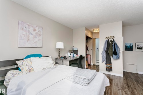 Bedroom featuring dark wood-type flooring, a closet, a textured ceiling, and ensuite bathroom - 407 8149 111 St S, Edmonton, AB - Indoor Photo Showing Bedroom