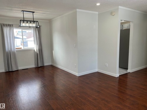 Unfurnished room featuring a textured ceiling, crown molding, dark wood finished floors, and suspended lighting - 10832 163 Street, Edmonton, AB - Indoor Photo Showing Other Room