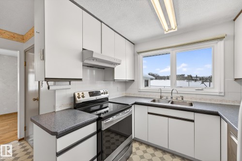 Kitchen featuring light flooring, stainless steel electric range, white cabinets, dark countertops, and a textured ceiling - 21 Marchand Place, St. Albert, AB - Indoor Photo Showing Kitchen With Double Sink