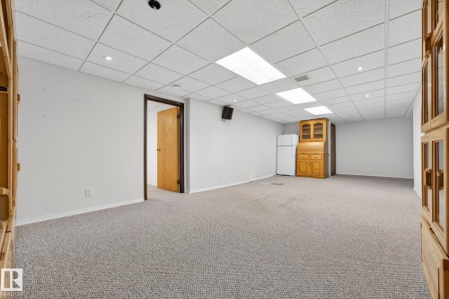 Finished basement featuring light colored carpet, freestanding refrigerator, and a paneled ceiling - 21 Marchand Place, St. Albert, AB - Indoor