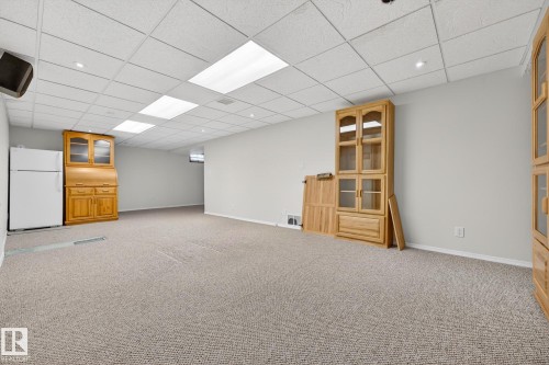 Finished below grade area with freestanding refrigerator, a drop ceiling, and light colored carpet - 21 Marchand Place, St. Albert, AB - Indoor