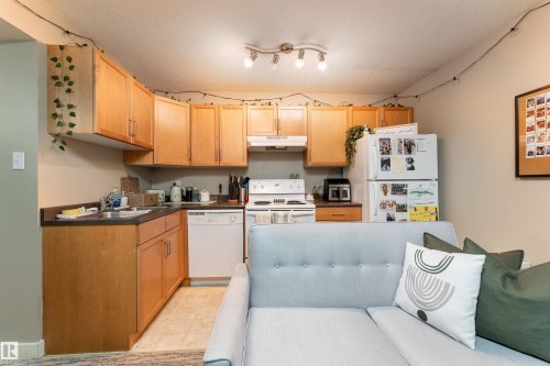 Kitchen featuring dark countertops, white appliances, and light wood finish cabinetry - 10906 72 Avenue, Edmonton, AB - Indoor Photo Showing Kitchen With Double Sink