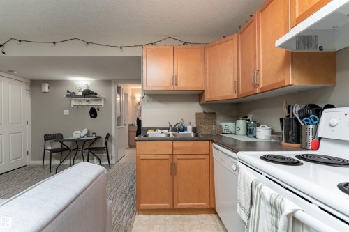 Kitchen with white appliances, ventilation hood, dark countertops, a textured ceiling, and light tile patterned floors - 10906 72 Avenue, Edmonton, AB - Indoor Photo Showing Kitchen With Double Sink