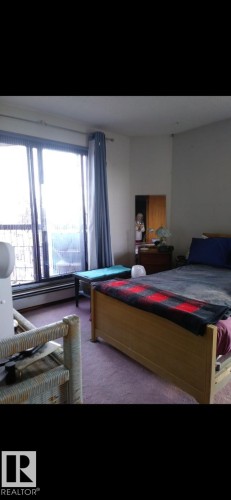 This room features a large window with vertical blinds and curtains, a baseboard heater, and carpeting - 401 10743 107 Street Nw, Edmonton, AB - Indoor Photo Showing Bedroom