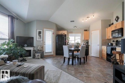 Living room featuring vaulted ceiling, dark stone finish floors, and a glass covered fireplace - 86 604 62 Street, Edmonton, AB - Indoor