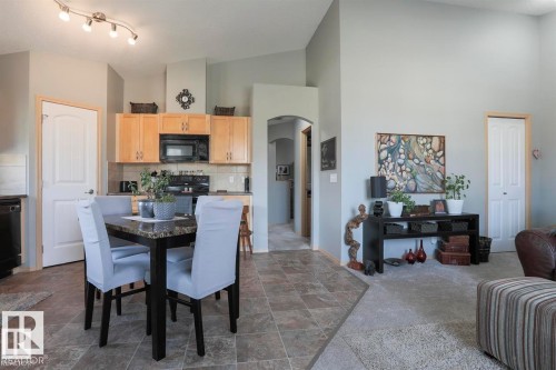 Dining area featuring arched walkways, dark stone finish flooring, lofted ceiling, and dark colored carpet - 86 604 62 Street, Edmonton, AB - Indoor