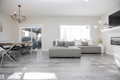Living area with suspended lighting, light wood-style flooring, and a glass covered fireplace - 15 Springbrook Wynd, Spruce Grove, AB - Indoor Photo Showing Living Room With Fireplace
