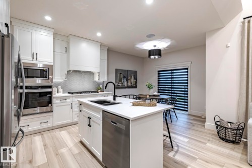 Kitchen with stainless steel appliances, white cabinetry, a center island with sink, light stone countertops, and a breakfast bar - 6275 180 Avenue, Edmonton, AB - Indoor Photo Showing Kitchen With Double Sink With Upgraded Kitchen