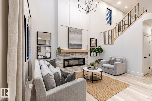 Living area with a high ceiling, light wood finished floors, a chandelier, and a fireplace - 6275 180 Avenue, Edmonton, AB - Indoor With Fireplace