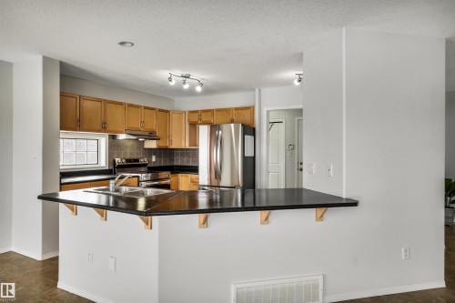 Kitchen with a kitchen breakfast bar, dark countertops, stainless steel appliances, wood finish cabinets, and a peninsula - 3401 47 Street, Beaumont, AB - Indoor Photo Showing Kitchen With Double Sink