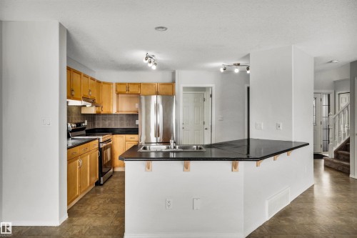 Kitchen with a kitchen breakfast bar, stainless steel appliances, a peninsula, and dark countertops - 3401 47 Street, Beaumont, AB - Indoor Photo Showing Kitchen With Double Sink