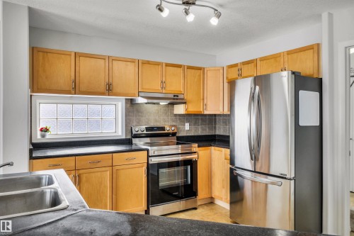Kitchen featuring stainless steel appliances, decorative backsplash, dark countertops, a textured ceiling, and light tile patterned flooring - 3401 47 Street, Beaumont, AB - Indoor Photo Showing Kitchen With Double Sink