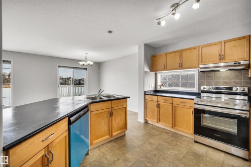 Kitchen featuring electric range, dark countertops, dishwasher, a chandelier, and tasteful backsplash - 3401 47 Street, Beaumont, AB - Indoor Photo Showing Kitchen With Double Sink