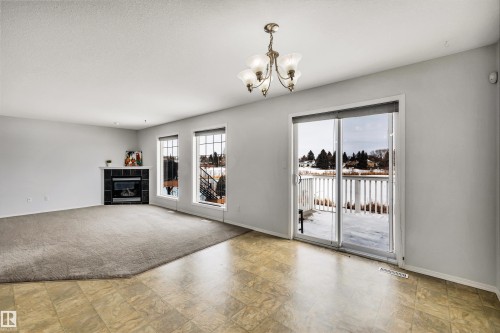 Unfurnished living room featuring a fireplace, suspended lighting, and light colored carpet - 3401 47 Street, Beaumont, AB - Indoor