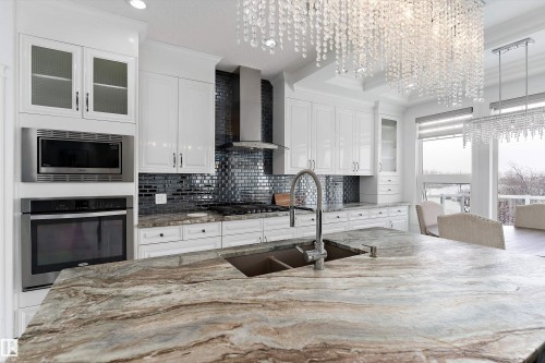 Kitchen with glass insert cabinets, light stone countertops, stainless steel appliances, a large island with sink, and crown molding - 1242 Starling Drive, Edmonton, AB - Indoor Photo Showing Kitchen