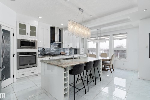 Kitchen with light stone counters, stainless steel appliances, tasteful backsplash, white cabinetry, and a breakfast bar area - 1242 Starling Drive, Edmonton, AB - Indoor Photo Showing Kitchen With Upgraded Kitchen