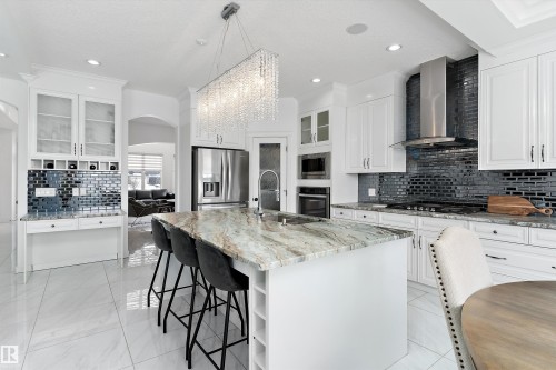 Kitchen with glass insert cabinets, tasteful backsplash, white cabinets, a breakfast bar, and light stone countertops - 1242 Starling Drive, Edmonton, AB - Indoor Photo Showing Kitchen With Upgraded Kitchen