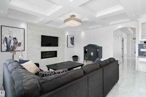 Living room featuring arched walkways, a stone fireplace, coffered ceiling, crown molding, and a chandelier - 1242 Starling Drive, Edmonton, AB - Indoor With Fireplace