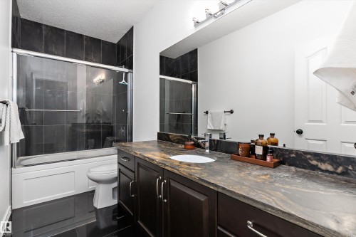 Full bathroom with vanity, a textured ceiling, shower / bath combination with glass door, and dark tile patterned flooring - 1242 Starling Drive, Edmonton, AB - Indoor Photo Showing Bathroom