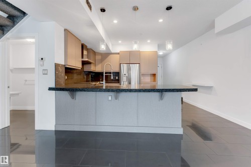 Kitchen featuring a kitchen bar, light wood finish cabinets, a peninsula, modern cabinets, and stainless steel fridge with ice dispenser - 102 10711 83 Avenue, Edmonton, AB - Indoor Photo Showing Kitchen With Upgraded Kitchen