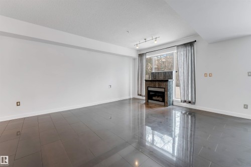 Unfurnished living room featuring a fireplace, a textured ceiling, and track lighting - 102 10711 83 Avenue, Edmonton, AB - Indoor With Fireplace