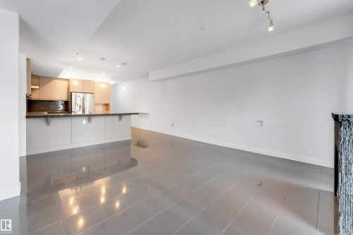 Kitchen featuring a breakfast bar, light wood finish cabinetry, a peninsula, stainless steel fridge with ice dispenser, and open floor plan - 102 10711 83 Avenue, Edmonton, AB - Indoor Photo Showing Kitchen