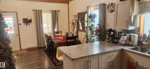 Kitchen featuring wooden walls, healthy amount of natural light, a peninsula, and dark wood-type flooring - 5216 - 53 Avenue, Clyde, AB - Indoor