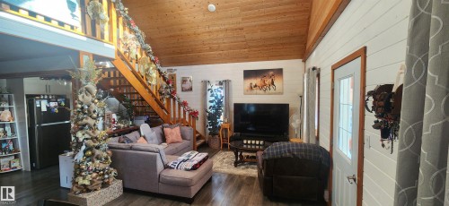 Living room with wooden walls, wood ceiling, dark wood-type flooring, stairs, and high vaulted ceiling - 5216 - 53 Avenue, Clyde, AB - Indoor