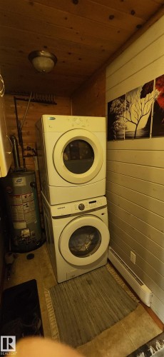Laundry area with wood walls, stacked washer / drying machine, water heater, and wood ceiling - 5216 - 53 Avenue, Clyde, AB - Indoor Photo Showing Laundry Room