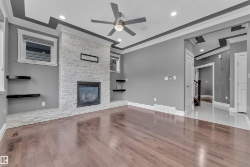 Unfurnished living room featuring a stone fireplace, a ceiling fan, ornamental molding, wood finished floors, and recessed lighting - 2612 Adam Court Sw, Edmonton, AB - Indoor With Fireplace