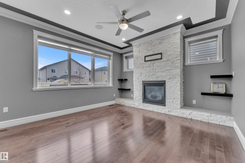 Unfurnished living room featuring crown molding, a ceiling fan, dark wood-type flooring, and a stone fireplace - 2612 Adam Court Sw, Edmonton, AB - Indoor Photo Showing Living Room With Fireplace