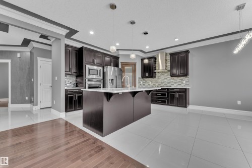 Kitchen with crown molding, a kitchen bar, stainless steel appliances, dark wood finish cabinets, and a center island with sink - 2612 Adam Court Sw, Edmonton, AB - Indoor Photo Showing Kitchen With Upgraded Kitchen