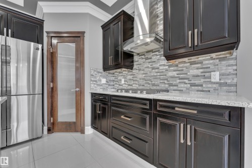 Kitchen featuring crown molding, stainless steel appliances, light stone counters, light tile patterned flooring, and dark wood finish cabinets - 2612 Adam Court Sw, Edmonton, AB - Indoor