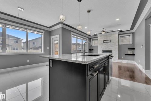Kitchen featuring dark cabinets, light tile patterned flooring, a textured ceiling, light stone countertops, and a stone fireplace - 2612 Adam Court Sw, Edmonton, AB - Indoor Photo Showing Kitchen With Upgraded Kitchen