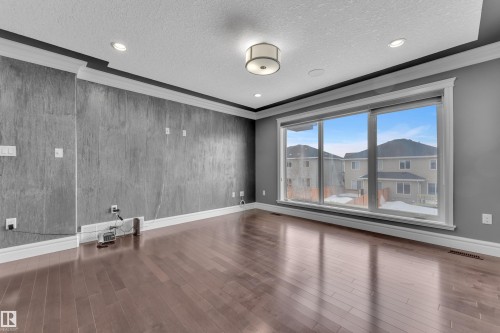 Empty room featuring a textured ceiling, crown molding, dark wood-type flooring, wooden walls, and recessed lighting - 2612 Adam Court Sw, Edmonton, AB - Indoor Photo Showing Other Room