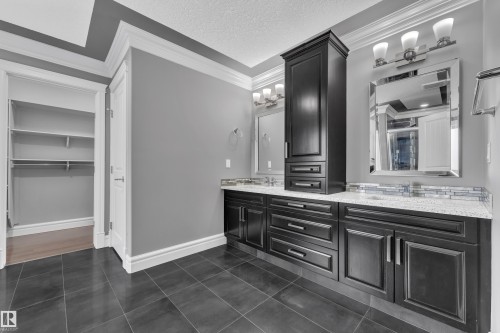 Full bath featuring double vanity, a textured ceiling, crown molding, and dark tile patterned floors - 2612 Adam Court Sw, Edmonton, AB - Indoor Photo Showing Bathroom