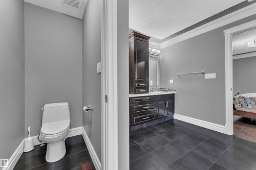 Full bathroom with a textured ceiling, vanity, ensuite bathroom, dark tile patterned flooring, and crown molding - 2612 Adam Court Sw, Edmonton, AB - Indoor Photo Showing Bathroom