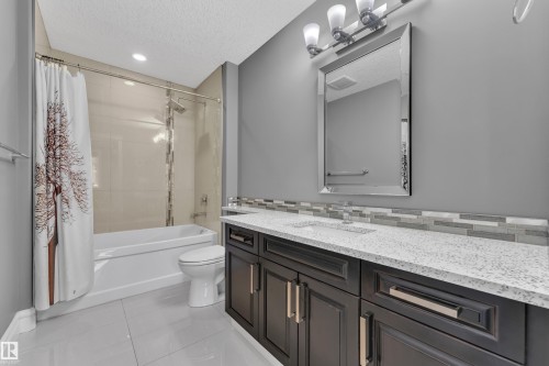 Bathroom featuring vanity, light tile patterned flooring, shower / bath combination with curtain, and a textured ceiling - 2612 Adam Court Sw, Edmonton, AB - Indoor Photo Showing Bathroom