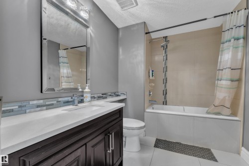Full bath featuring tiled shower / bath, vanity, a textured ceiling, light tile patterned floors, and backsplash - 2612 Adam Court Sw, Edmonton, AB - Indoor Photo Showing Bathroom