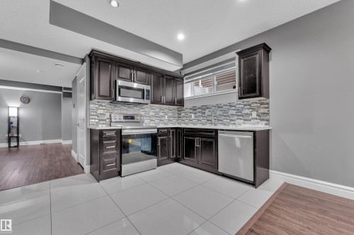 Kitchen with stainless steel appliances, light tile patterned floors, dark wood finish cabinets, and tasteful backsplash - 2612 Adam Court Sw, Edmonton, AB - Indoor Photo Showing Kitchen With Upgraded Kitchen