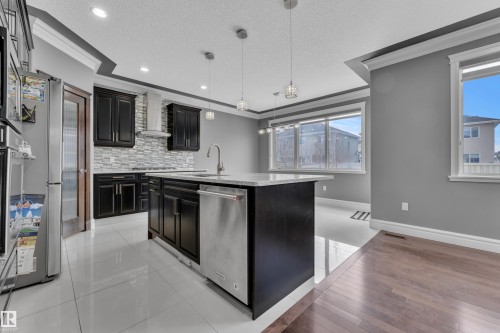 Kitchen featuring ornamental molding, a center island with sink, stainless steel appliances, a textured ceiling, and hanging light fixtures - 2612 Adam Court Sw, Edmonton, AB - Indoor Photo Showing Kitchen With Upgraded Kitchen