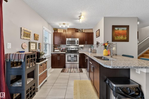 Kitchen featuring a peninsula, stainless steel appliances, tasteful backsplash, light stone counters, and light tile patterned flooring - 14 1140 Chappelle Boulevard, Edmonton, AB - Indoor Photo Showing Kitchen With Double Sink With Upgraded Kitchen