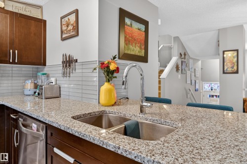 Kitchen with decorative backsplash, a textured ceiling, light stone counters, and dark wood finish cabinets - 14 1140 Chappelle Boulevard, Edmonton, AB - Indoor Photo Showing Kitchen With Double Sink With Upgraded Kitchen