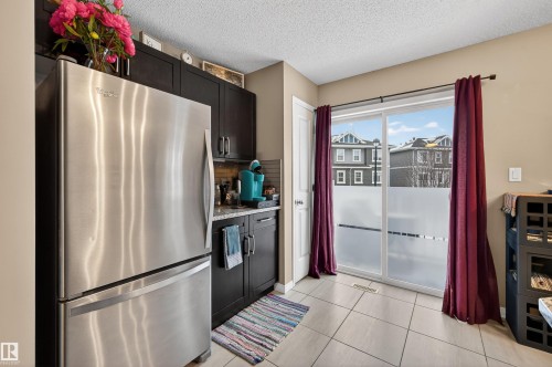 Kitchen with freestanding refrigerator, a textured ceiling, light stone counters, light tile patterned floors, and backsplash - 14 1140 Chappelle Boulevard, Edmonton, AB - Indoor