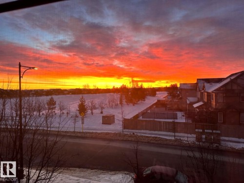 The property offers striking views of a vibrant sunset over a snow-covered landscape, featuring scattered trees and a street light - 14 1140 Chappelle Boulevard, Edmonton, AB - Outdoor With View